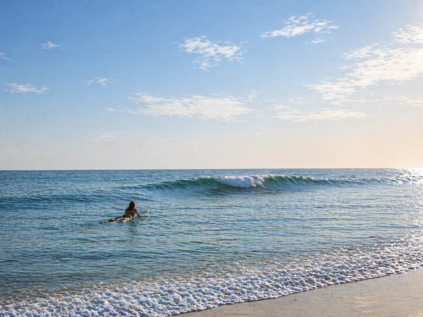 A surfer paddling into a glassy wave off Playa Roca, sunlight rim-lighting the silhouette.